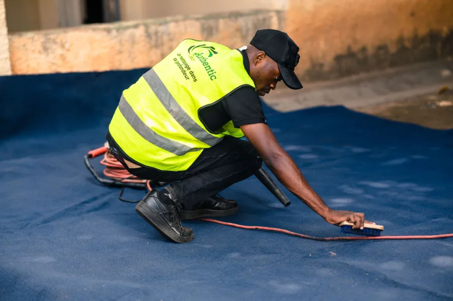 Spring - A worker dressed in a safety vest cleans a blue carpet outdoors with a brush